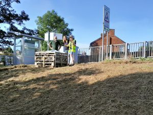 Volunteers stand next to the bug hotel at Derby Road station after raking the wildflower meadow